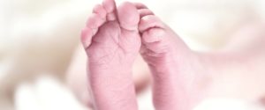 Close-up of a parent holding a baby's bare feet, representing foot health from an early age